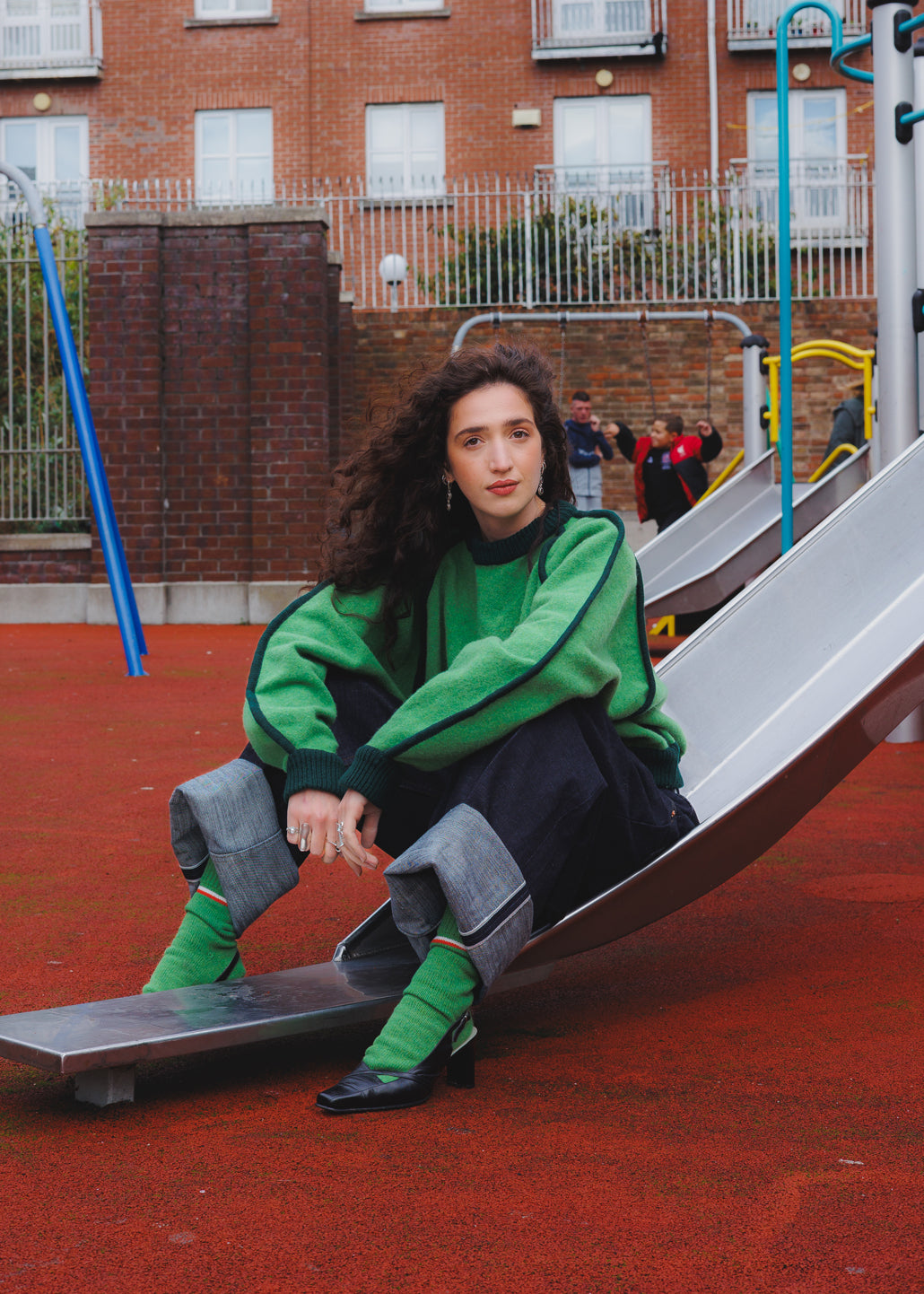 Woman in a grass green lambs wool jumper sitting on a playground. she is also wearing lambs wool socks in a vibrant green 